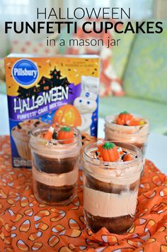 three halloween cupcakes in mason jars on an orange tablecloth with the box behind them