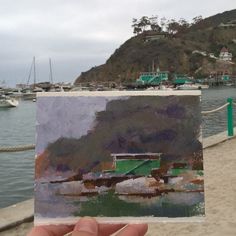 a person holding up a piece of paper with water and boats in the back ground