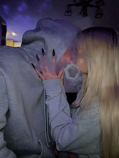 a woman with long blonde hair wearing a grey hoodie and holding her hands to her face