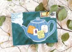 a teapot with tags attached to it sitting on a lace covered table cloth next to some leaves