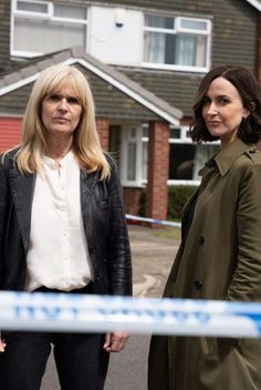 two women standing next to each other in front of a police cord and house behind them