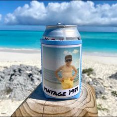 a beer can sitting on top of a piece of wood near the ocean and beach