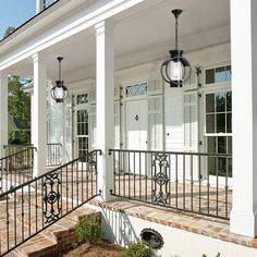 a white house with black iron railings on the front porch and stairs leading up to it