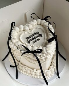 a heart shaped cake with black ribbon around it on a white plate in a box