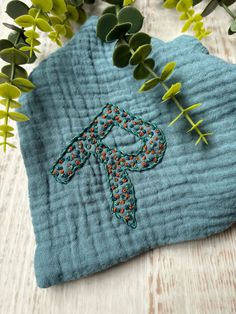 a blue towel with an embroidered cross on it next to some green leaves and flowers