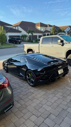 two black cars parked next to each other on a brick road in front of houses