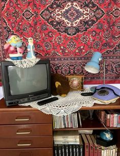 an old tv sitting on top of a wooden dresser next to a wall hanging tapestry