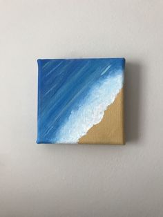 a small painting on a white wall with blue and yellow waves in the ocean behind it