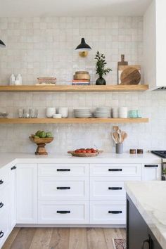 a white kitchen with open shelving and lots of bowls on the counter top,