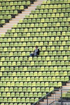 a man sitting in the middle of a stadium filled with green seats and looking at his cell phone