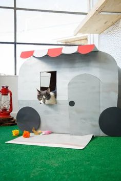 a cat sitting inside of a small gray elephant shaped house on top of green carpet