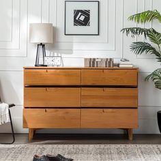 a wooden dresser sitting next to a plant in a living room on top of a rug