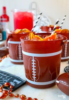 two football themed cups filled with oranges and ice on a table next to candy