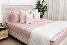 a bed with pink sheets and pillows on top of it next to a night stand