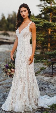 a woman in a white wedding dress standing on rocks near the water and holding a bouquet