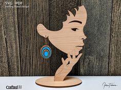 a wooden cutout of a woman's face with earrings on it, against a wood background