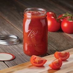 a jar filled with tomato sauce sitting on top of a wooden cutting board next to sliced tomatoes