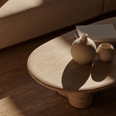 two white vases sitting on top of a wooden table next to a book and a couch