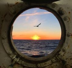 the sun is setting over the ocean through a porthole in an old ship's hull