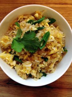 a white bowl filled with rice and greens on top of a wooden table next to a fork