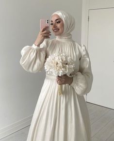 a woman taking a selfie wearing a white dress and holding a bouquet of flowers