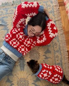 a woman laying on top of a rug next to a cat wearing knitted sweaters