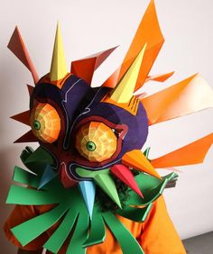 an origami mask made out of orange, green and purple paper with spikes on it