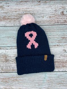 a knitted beanie with pink and blue designs on it sitting on a wooden surface