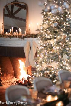 a decorated christmas tree in front of a fire place with candles on the mantel