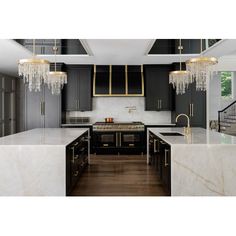 a kitchen with black cabinets and white marble counter tops, gold accents on the chandelier