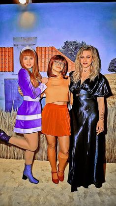 three women standing next to each other in front of a wall with a painting on it