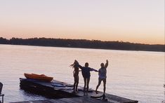 three girls standing on a dock with their arms in the air