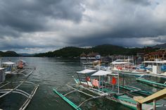 many boats are docked in the water under a cloudy sky