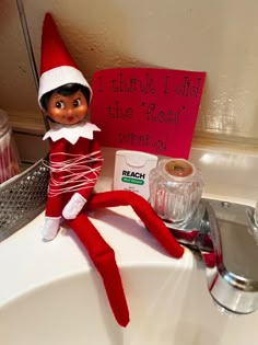 an elf sitting on top of a sink next to a sign