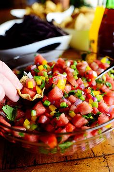 a person scooping salsa into a bowl with tortilla chips on the side