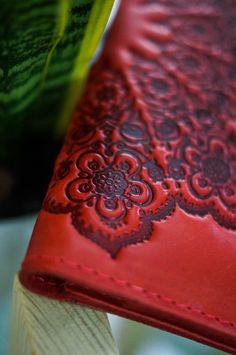 a red leather wallet sitting on top of a wooden table next to a potted plant