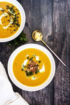 two bowls of carrot soup on a wooden table with spoons and napkin next to them