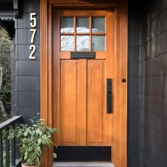 a wooden door on the side of a black house with a plant in front of it