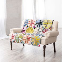 a couch with a colorful quilt on it in front of a white curtained window