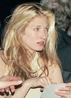 a woman with long blonde hair is looking at something in her hand as she sits next to other people