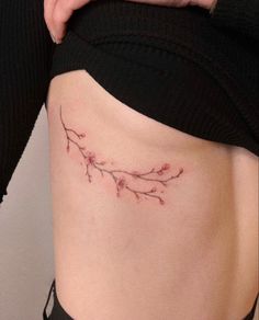 a woman's stomach with a small branch tattoo on her lower side ribcage