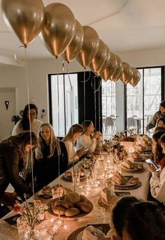 a group of people sitting at a long table with balloons and candles in the air