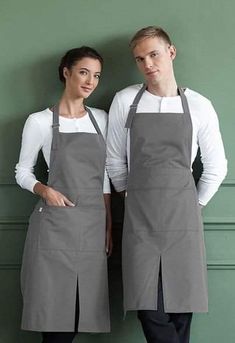 two people standing next to each other wearing grey aprons and white shirts with their hands on their hips