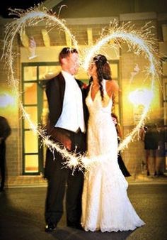 a newly married couple standing in front of a building with sparklers forming the shape of a heart