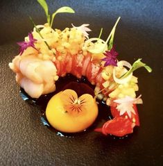 an assortment of sushi on a black plate with flowers and fruit in the center