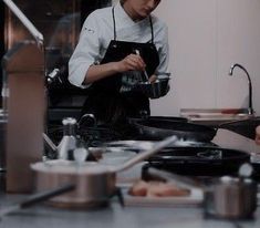 the woman is cooking in the kitchen with an apron on and she is looking at her phone