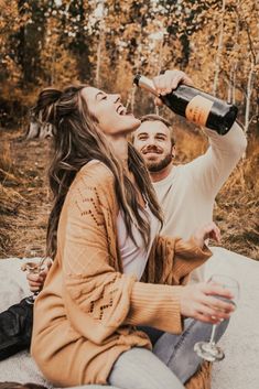 a man and woman sitting on the ground drinking from wine bottles while they look at each other