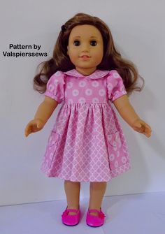 a doll with brown hair wearing a pink dress and pink shoes, standing against a white wall