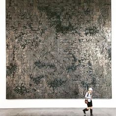 a woman standing in front of a large painting on the side of a white wall