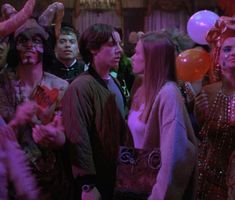 a group of people standing around each other with balloons in the air and clown makeup on their faces